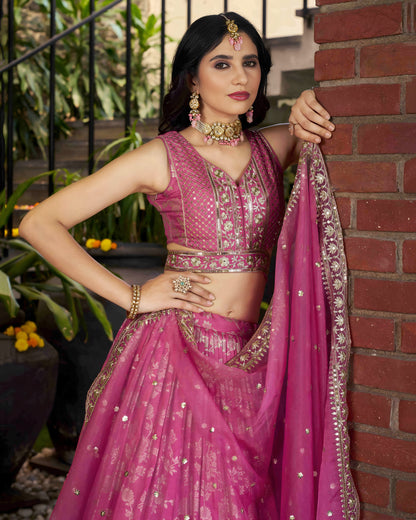 Woman in a pink traditional outfit standing against a brick wall.