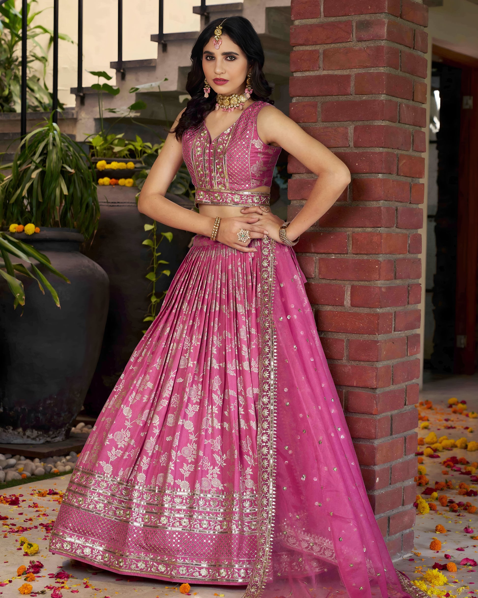 Woman in a pink traditional outfit standing against a brick wall.