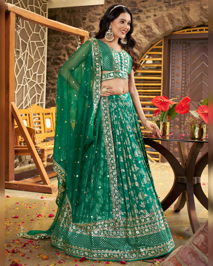 Woman in a green traditional outfit standing in an indoor setting with decorative elements.