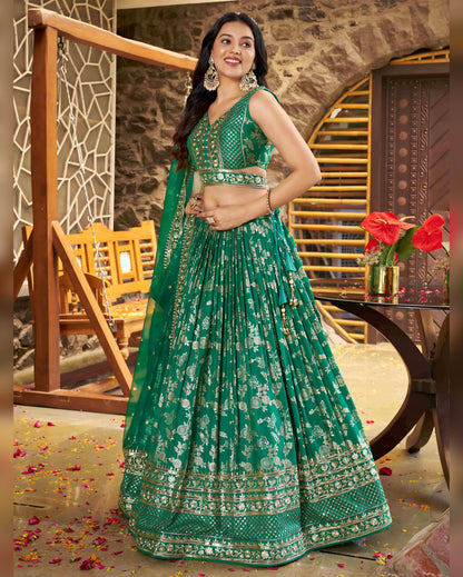 Woman in a green traditional outfit standing in an indoor setting with decorative elements.