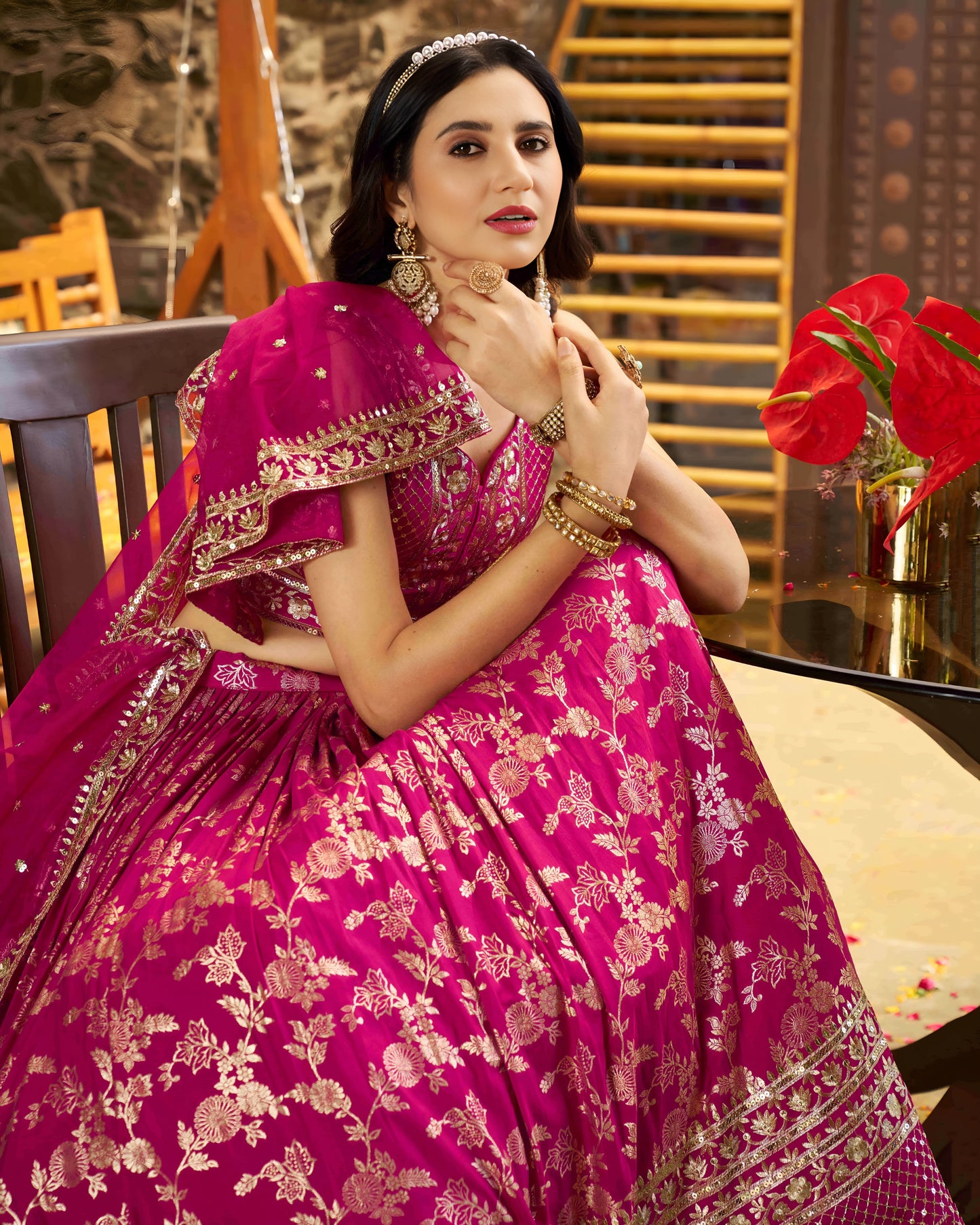 Woman in a pink traditional outfit with gold embroidery, sitting indoors.