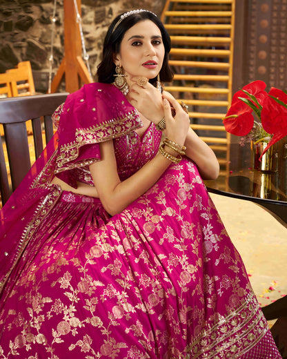 Woman in a pink traditional outfit with gold embroidery, sitting indoors.