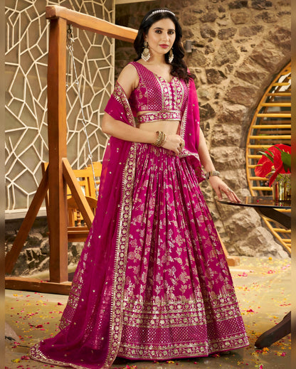 Woman in a pink traditional outfit with intricate designs in an indoor setting.