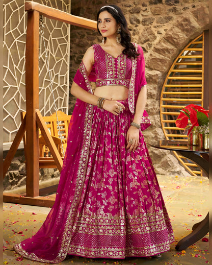 Woman in a pink embroidered traditional outfit standing indoors with decorative elements.