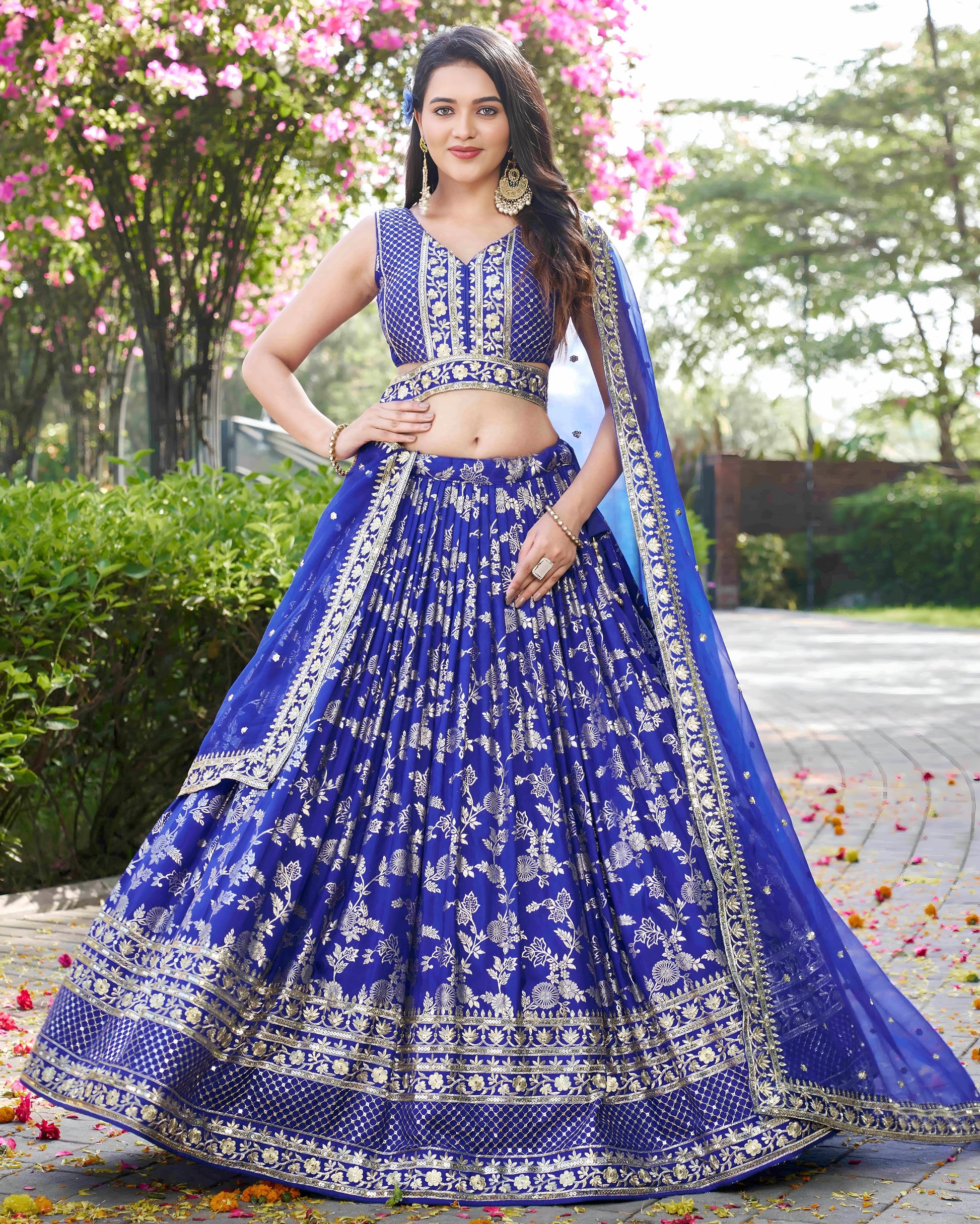 Woman in a blue embroidered traditional outfit standing outdoors with greenery in the background
