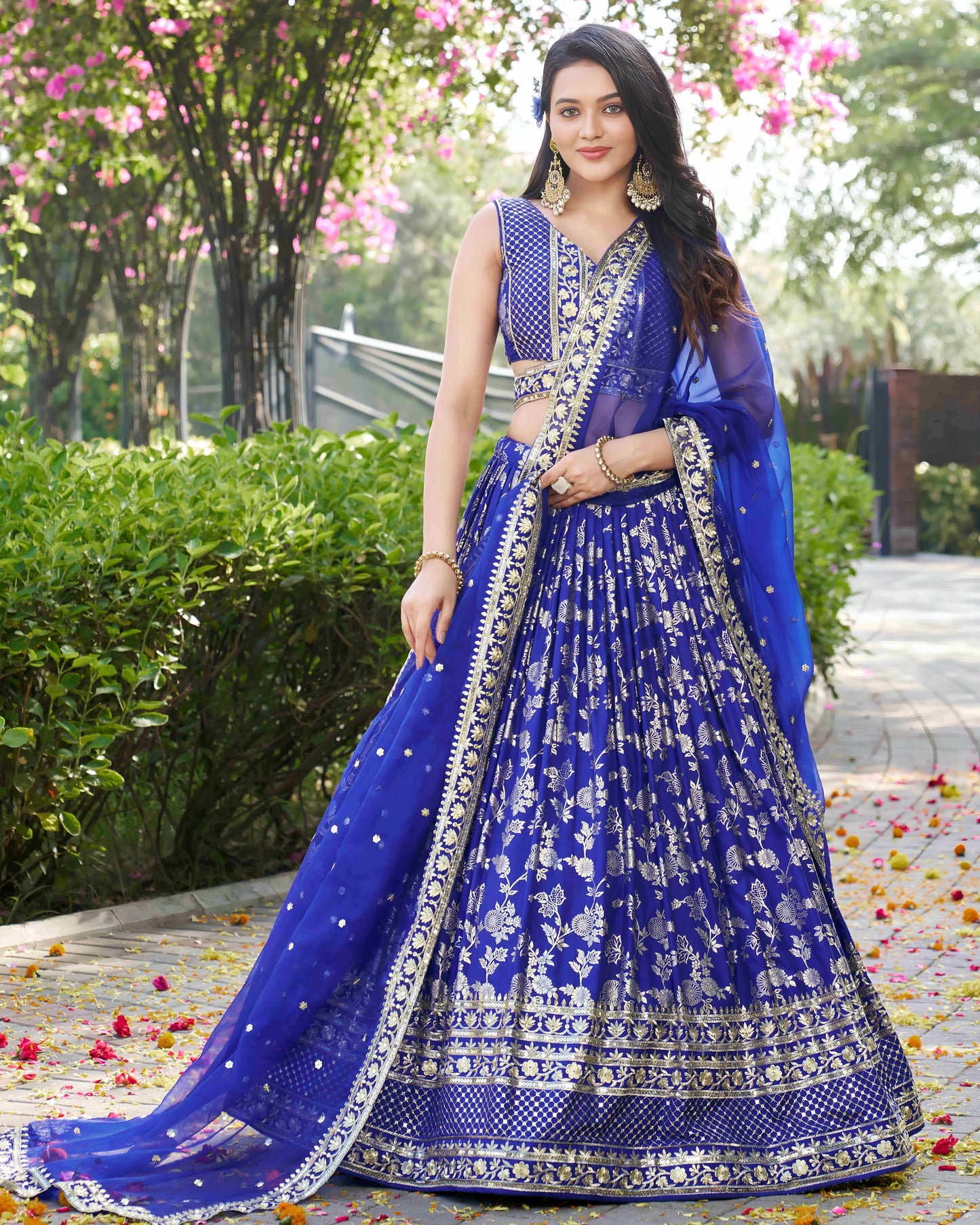 Woman in a blue embroidered lehenga standing outdoors with greenery in the background
