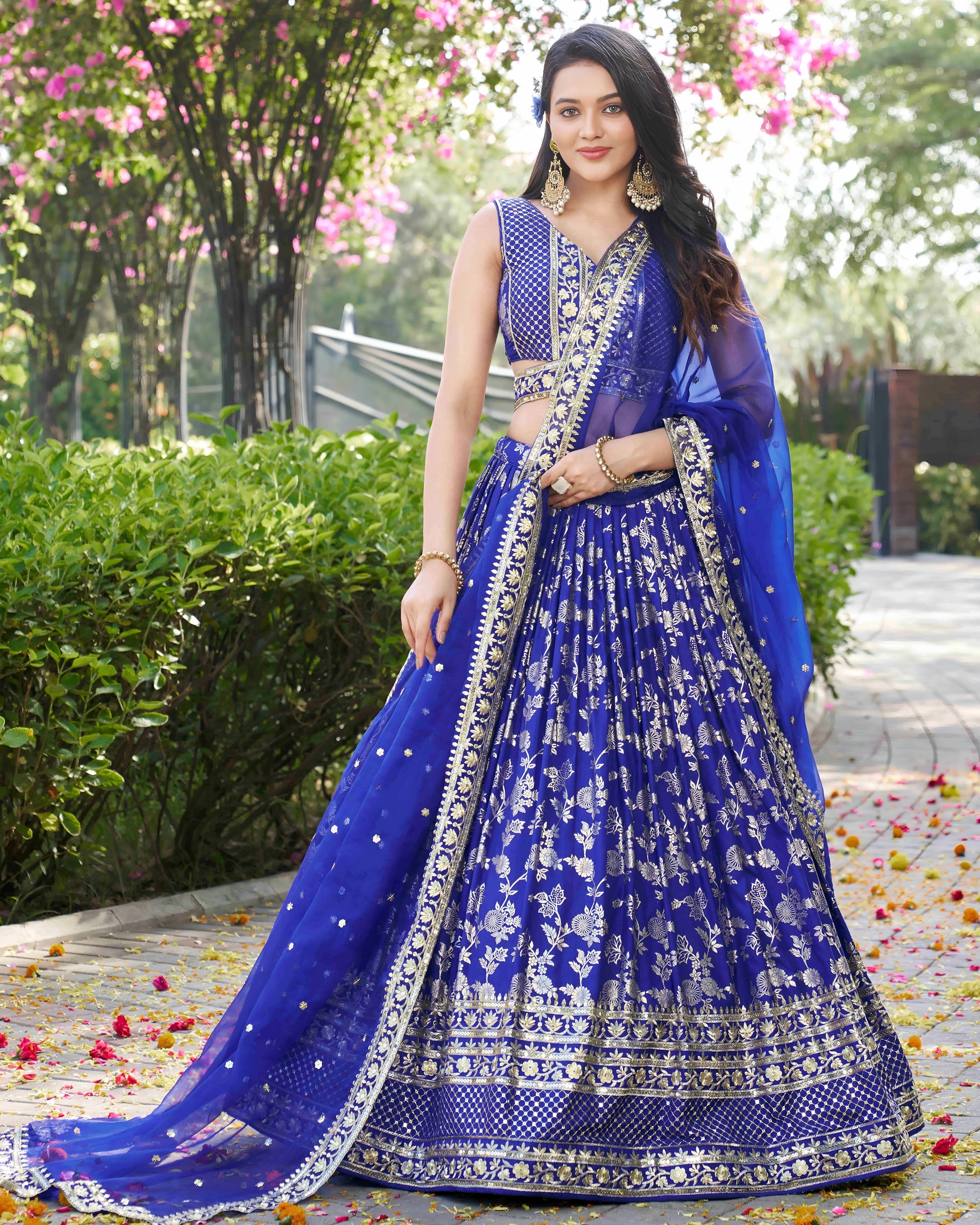 Woman in a blue embroidered lehenga standing outdoors with greenery in the background