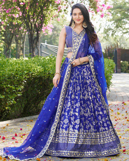 Woman in a blue embroidered lehenga standing outdoors with greenery in the background