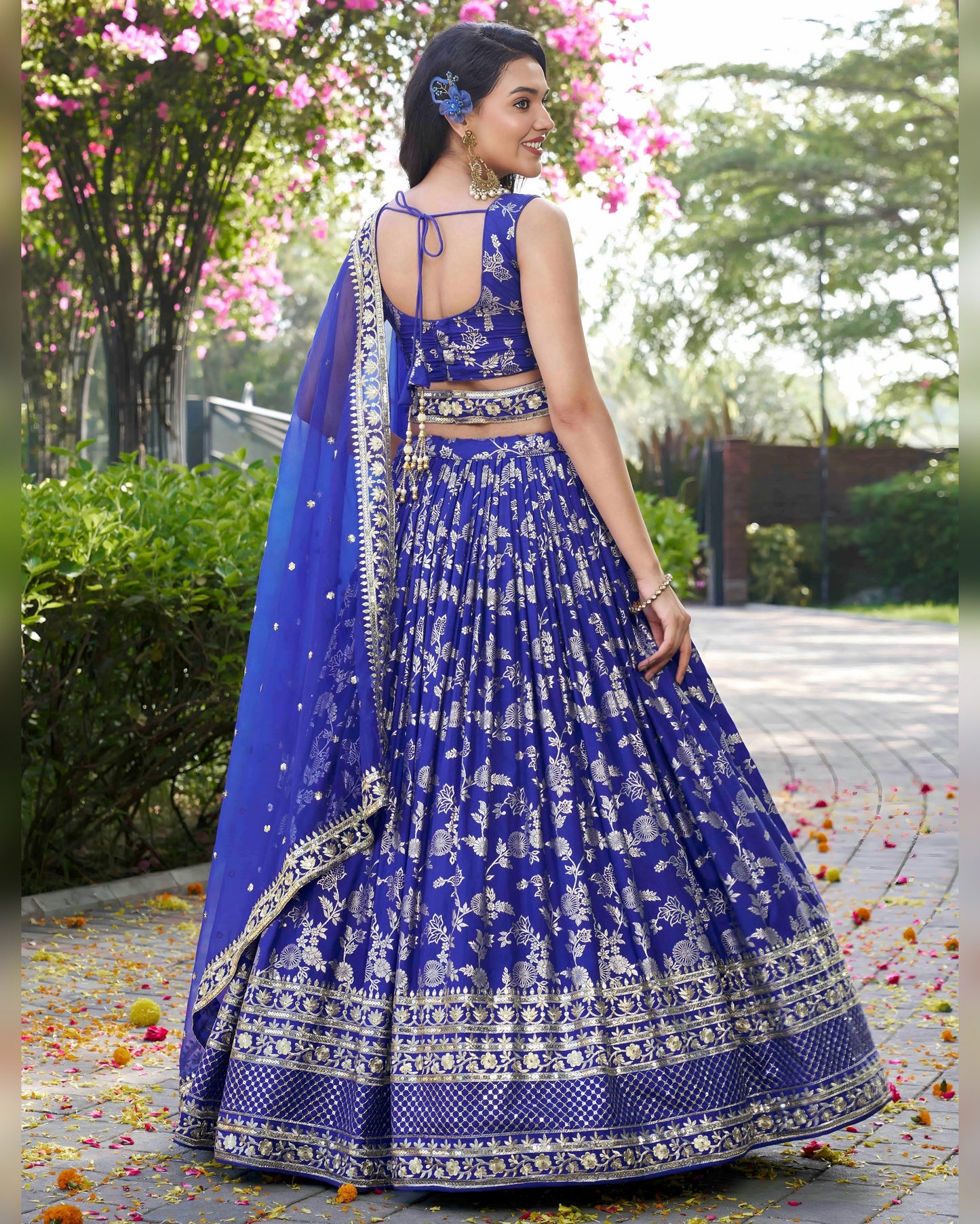 Woman in a blue and white embroidered traditional outfit standing outdoors with greenery in the background.
