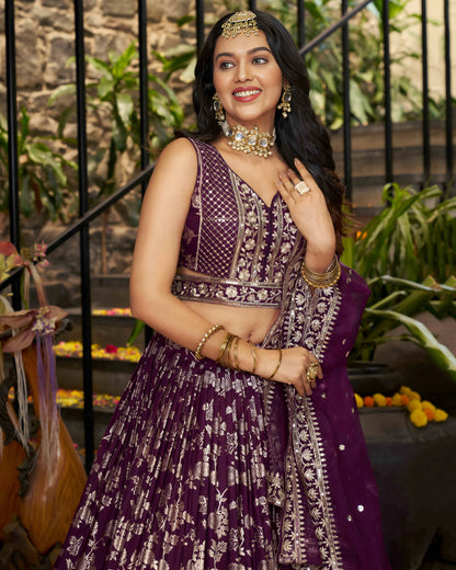 Woman in traditional purple and gold outfit with jewelry, standing outdoors.