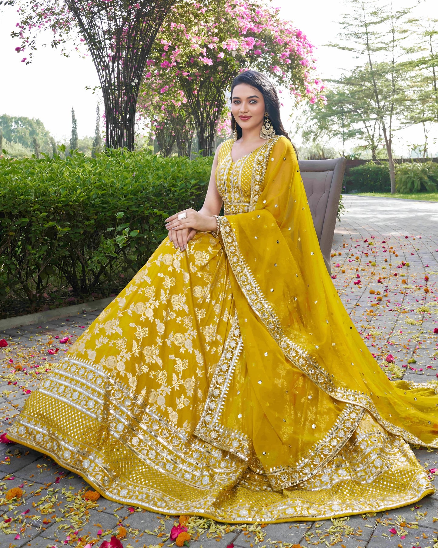 Woman in a yellow traditional outfit with floral decorations, sitting outdoors.