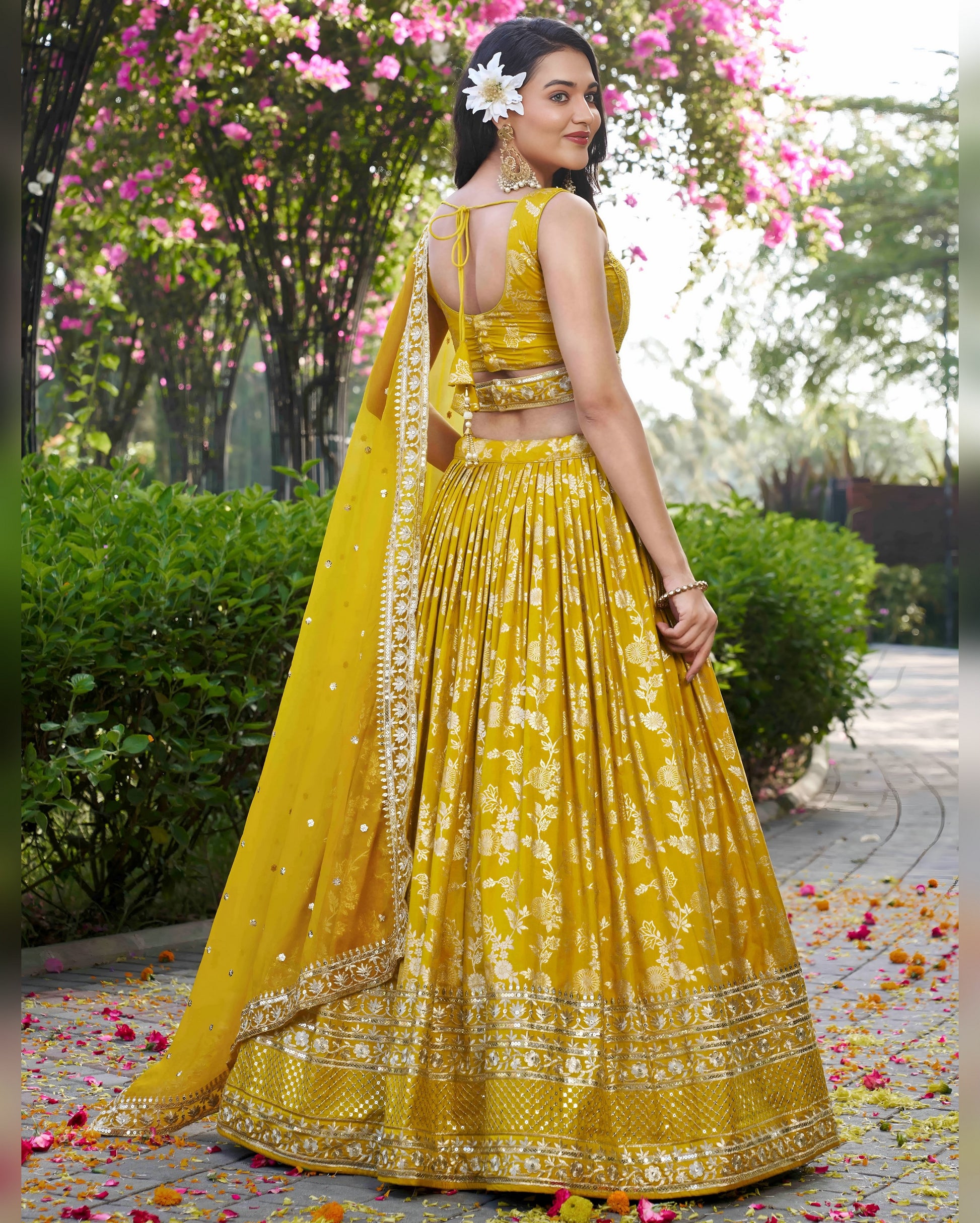Woman in a yellow traditional outfit with floral decorations in an outdoor setting.