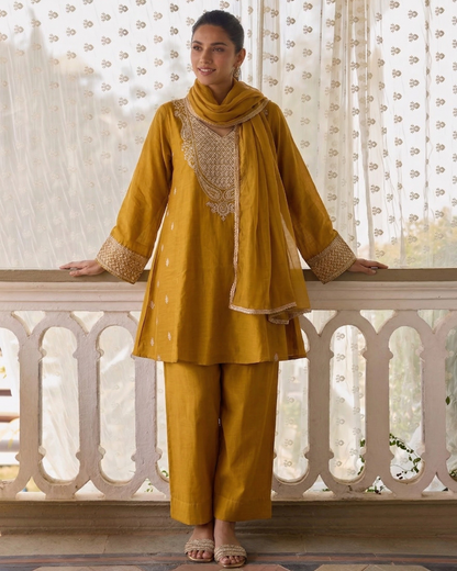Woman in mustard yellow traditional outfit with a dupatta, standing on a balcony.
