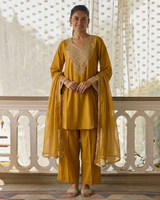 Woman wearing a mustard yellow traditional outfit with intricate detailing in a decorative setting.
