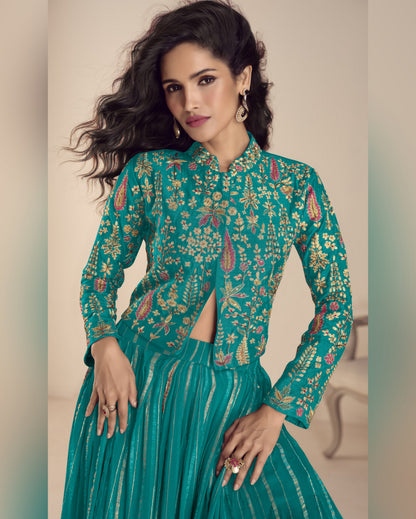 Woman wearing a teal embroidered outfit with a neutral background