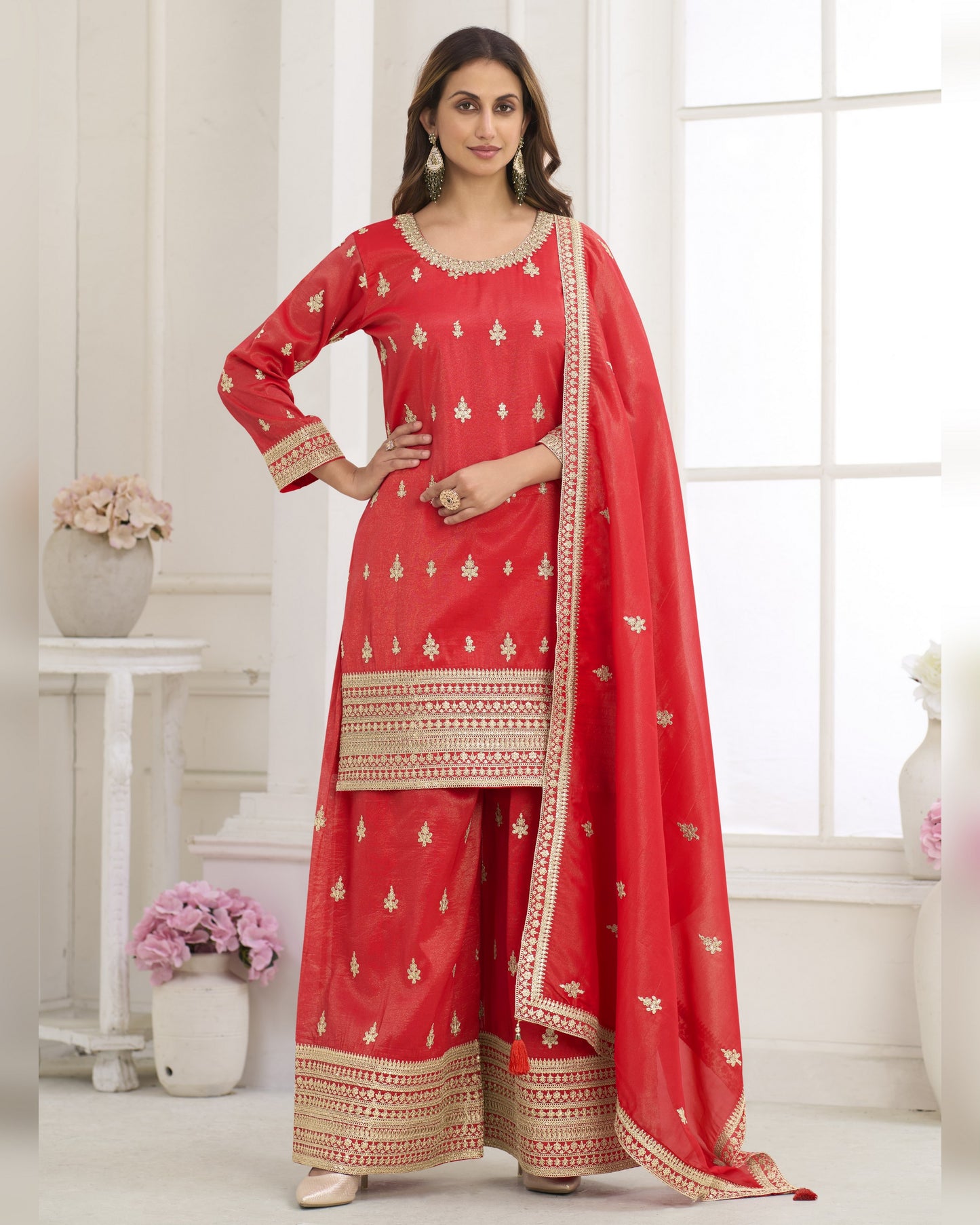 Woman wearing a red traditional outfit with gold embroidery in a bright room.