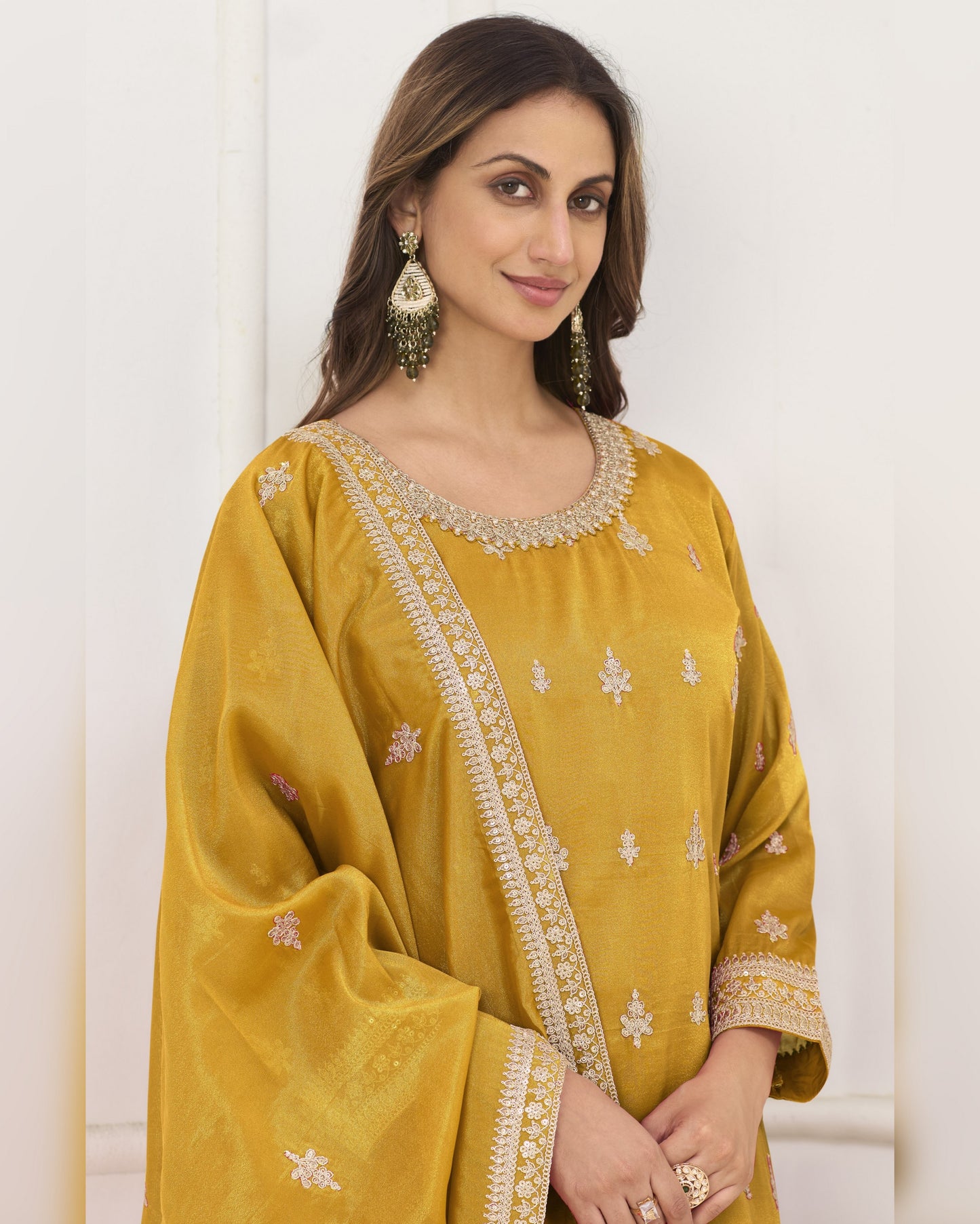 Woman wearing a mustard yellow traditional outfit with intricate designs on a white background