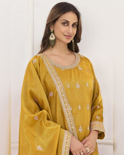 Woman wearing a mustard yellow traditional outfit with intricate designs on a white background