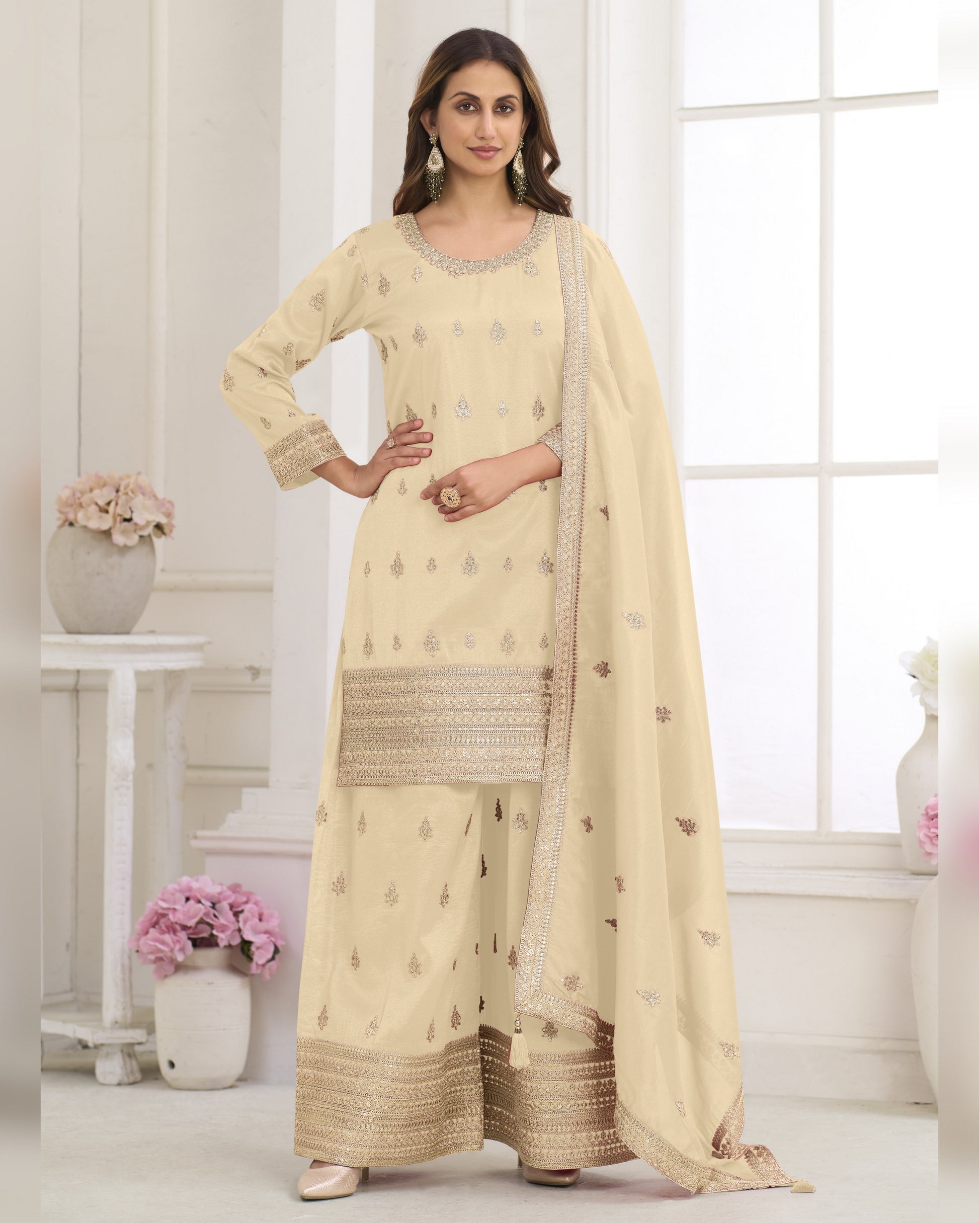 Woman wearing a beige traditional outfit with a matching dupatta in a bright room.