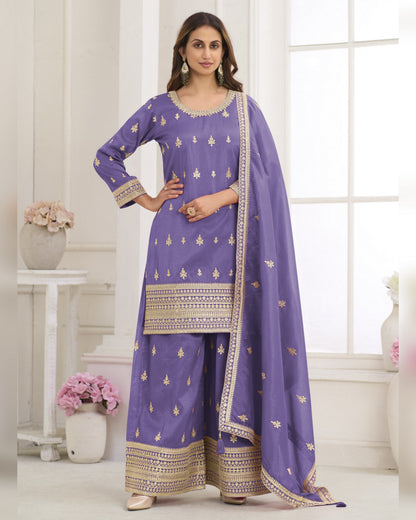Woman wearing a purple traditional outfit with gold patterns in a bright room.