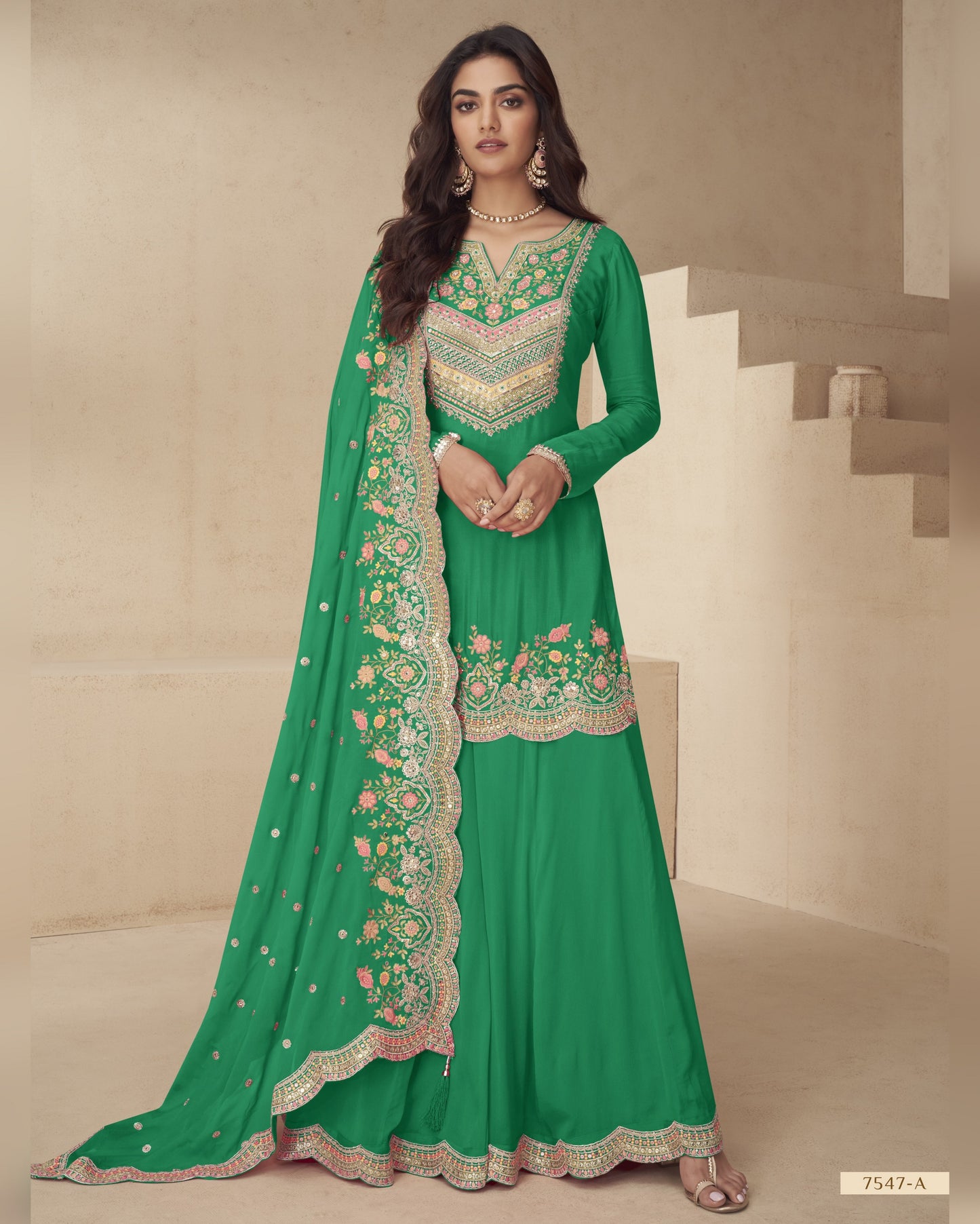 Woman wearing a green embroidered traditional outfit with a matching dupatta on a neutral background