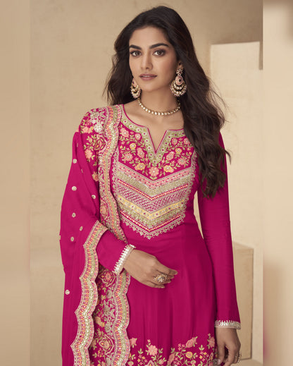 Woman wearing a pink embroidered traditional outfit with gold jewelry against a beige background