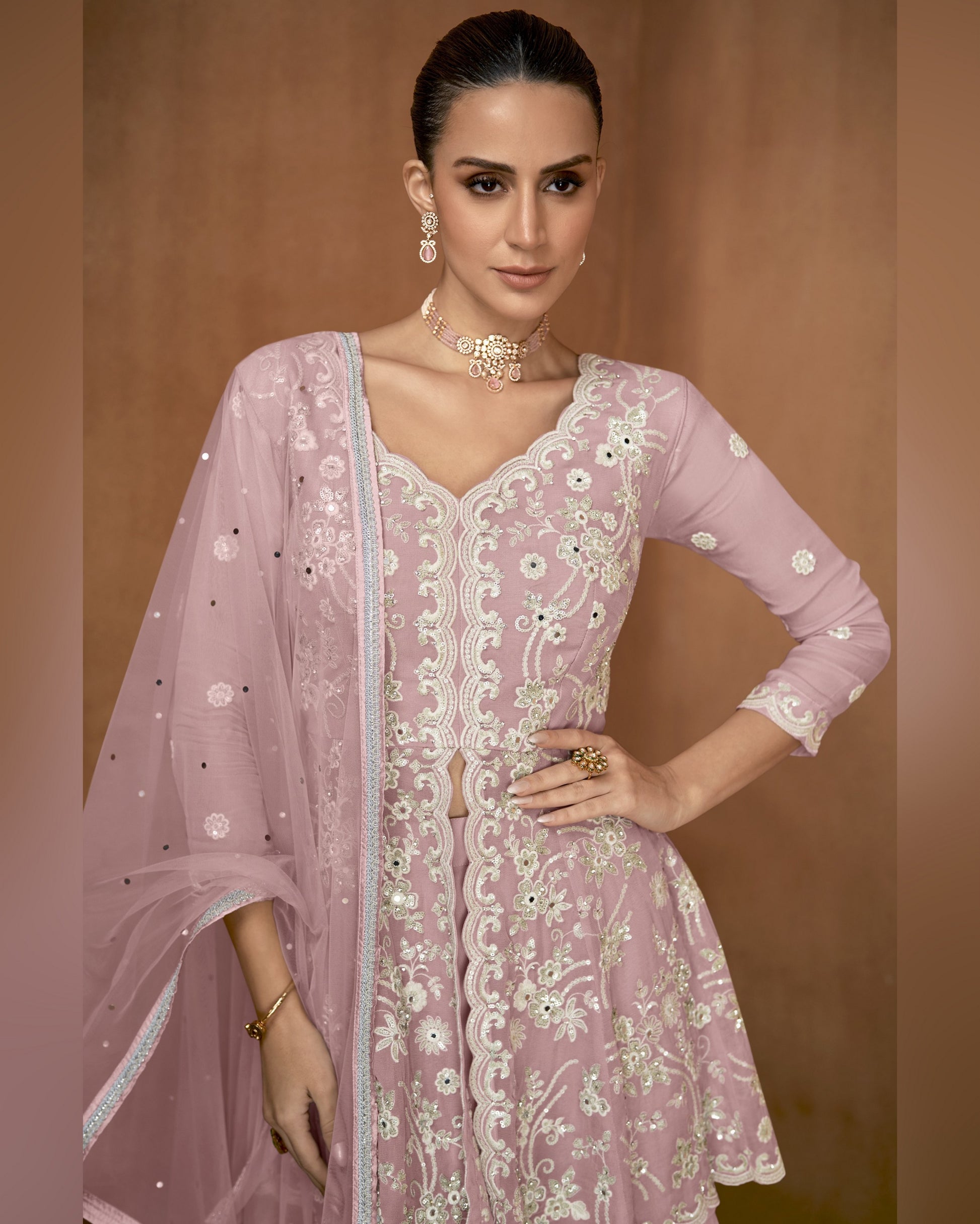 Woman wearing a pink embroidered traditional outfit with a matching dupatta on a brown background