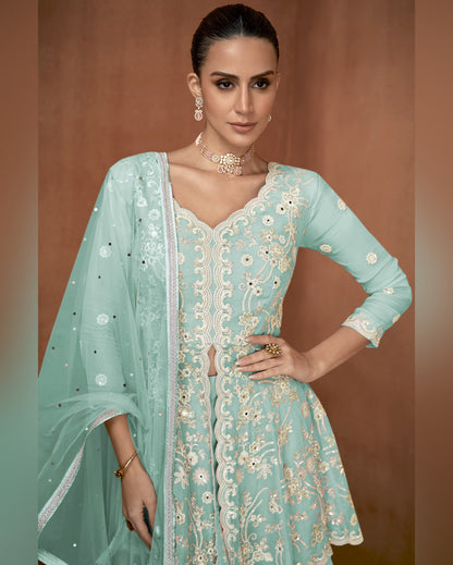 Woman wearing a light blue embroidered traditional outfit with a matching dupatta against a brown background