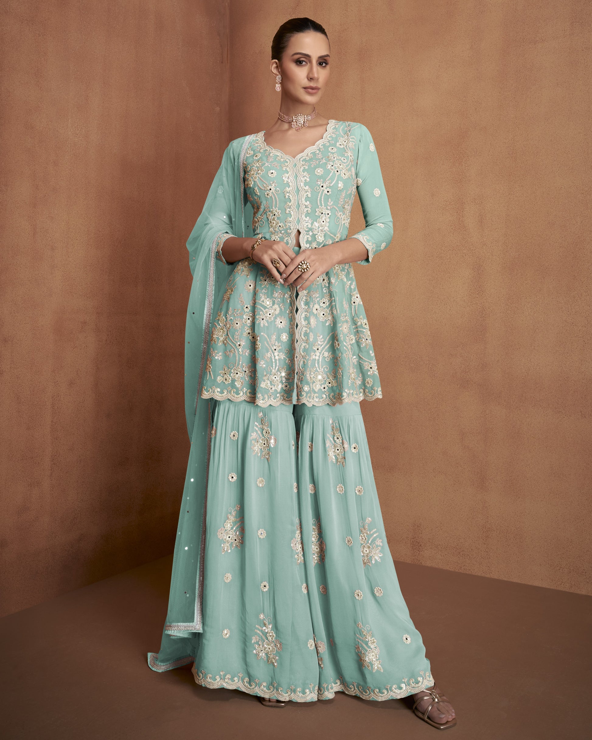 Woman wearing a light blue embroidered traditional outfit against a brown background