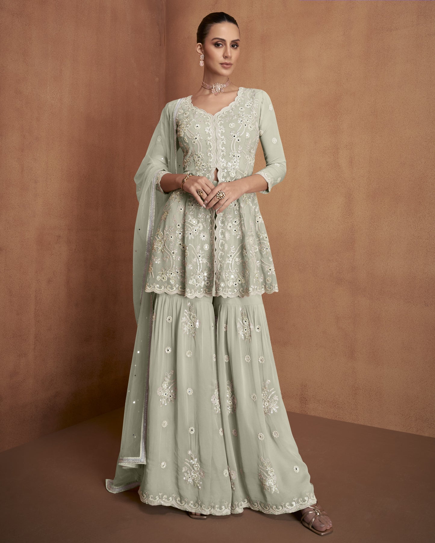 Woman wearing a light green embroidered traditional outfit against a brown background