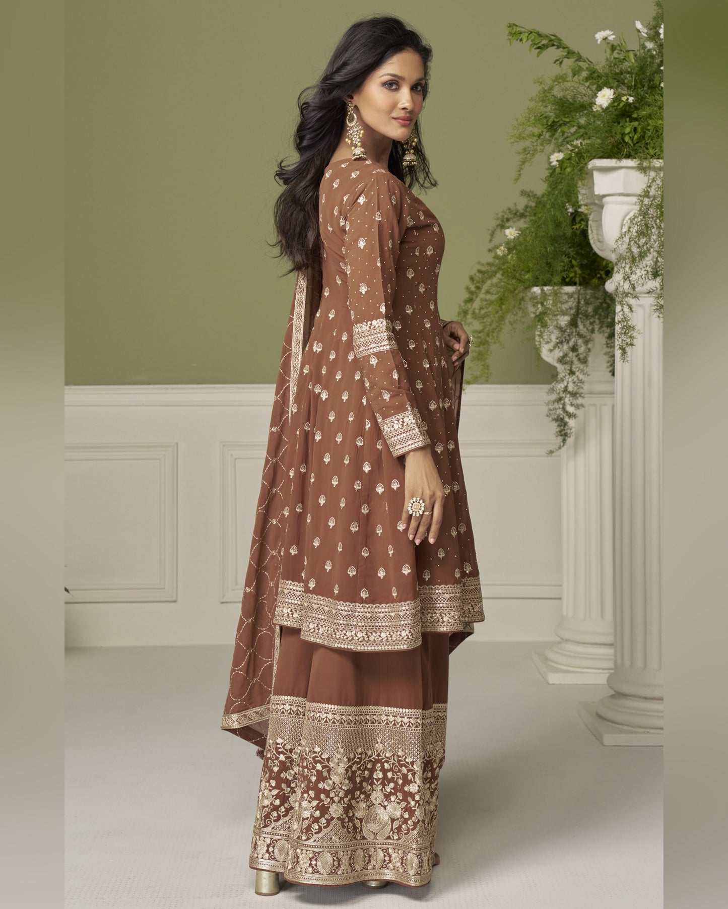 Woman wearing a brown embroidered traditional outfit in a decorated room.