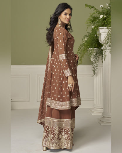 Woman wearing a brown embroidered traditional outfit in a decorated room.