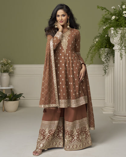 Woman in a brown embroidered traditional outfit standing in a decorated room with plants.