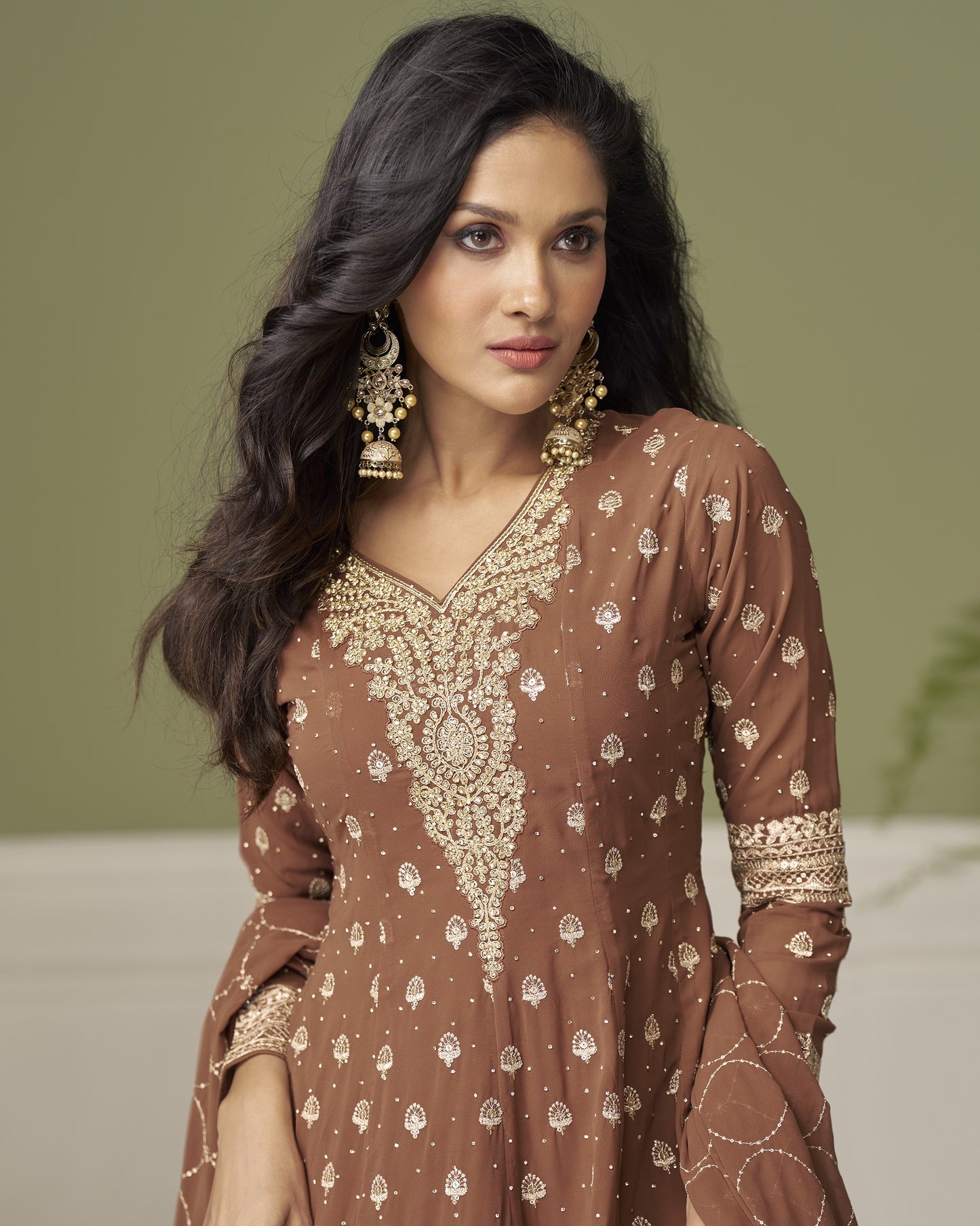 Woman wearing a brown patterned dress with gold accents against a neutral background