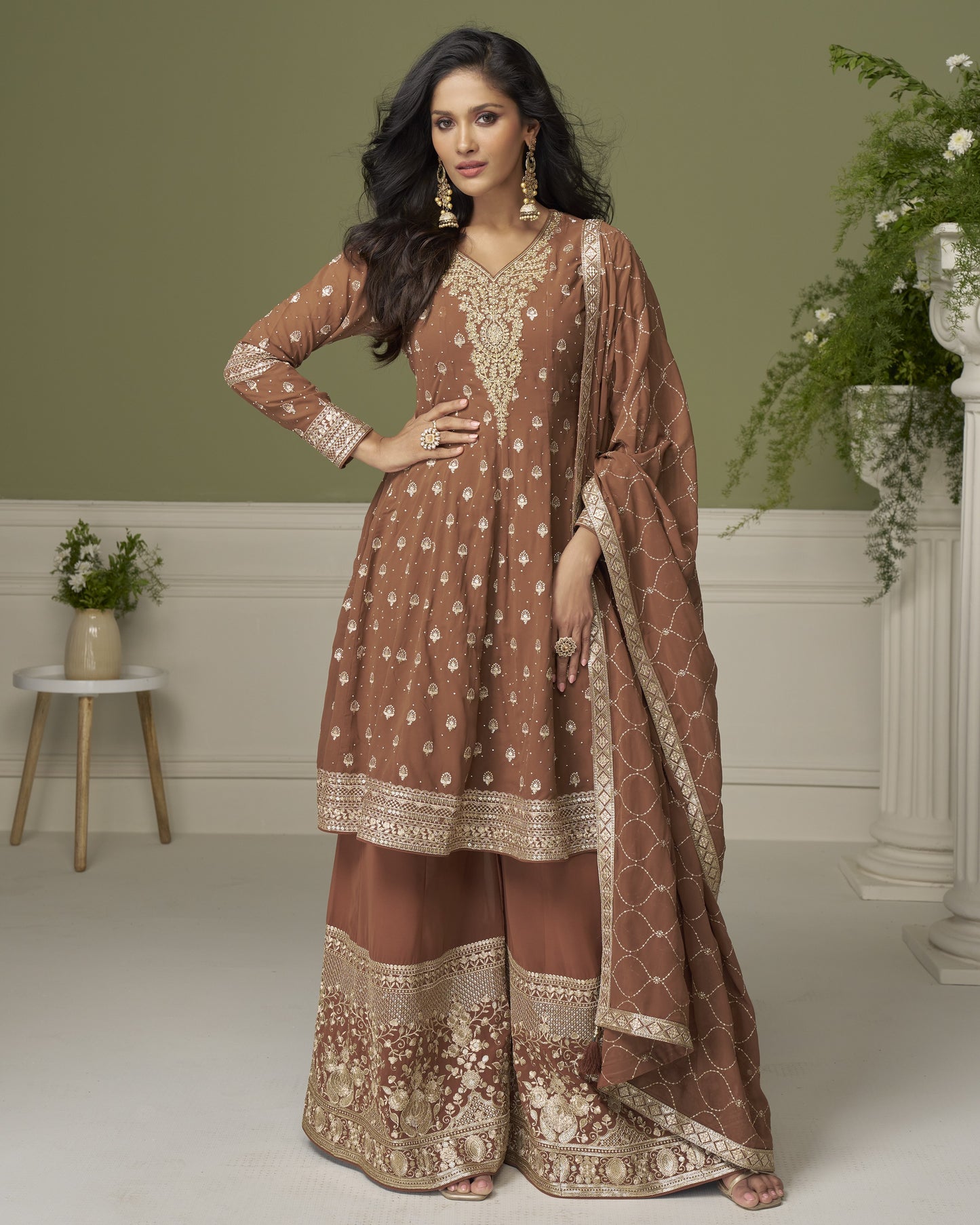 Woman wearing a brown and gold traditional outfit in a decorated room.