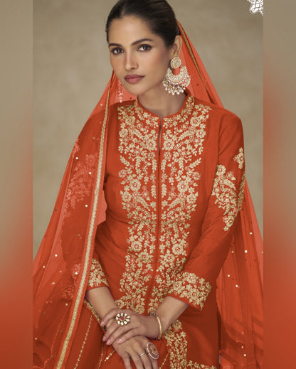 Woman wearing an orange embroidered traditional outfit with a matching dupatta.