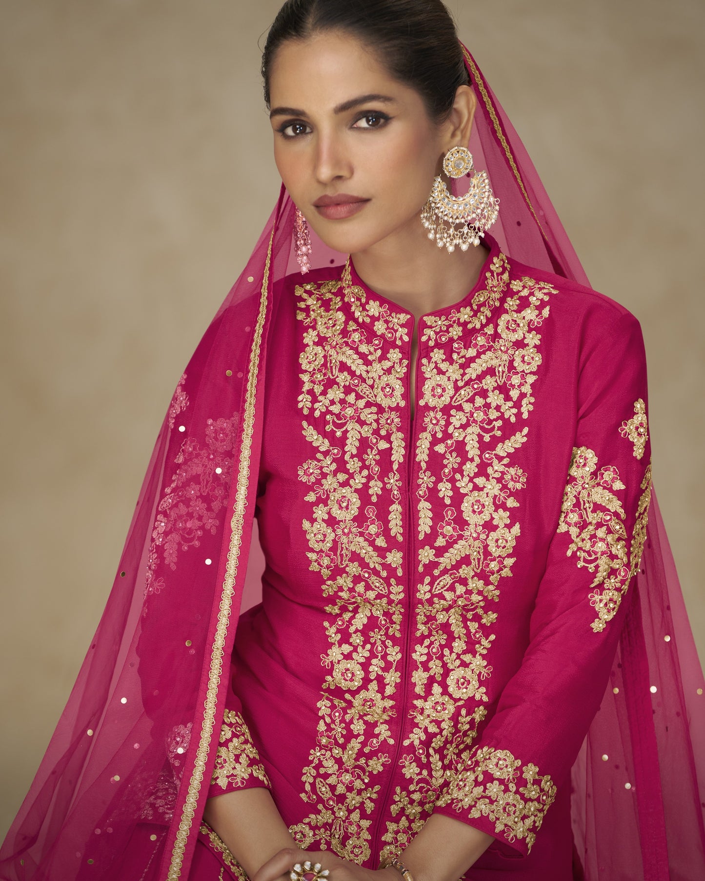 Woman wearing a pink embroidered outfit with a matching dupatta on a beige background