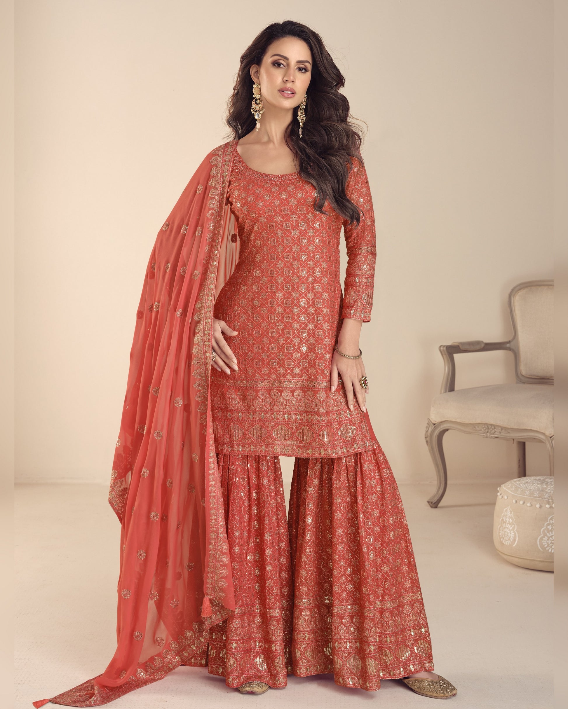 Woman wearing a red traditional outfit with a matching dupatta in a neutral setting