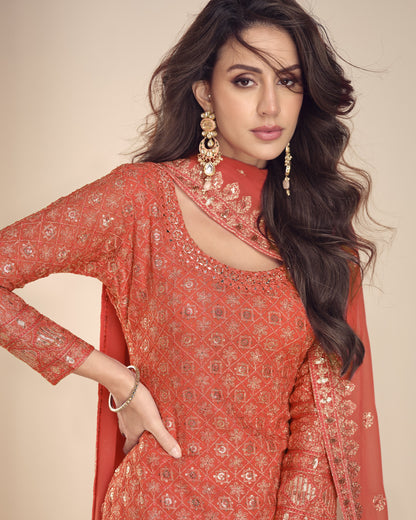 Woman wearing a red embroidered traditional outfit with gold jewelry against a beige background
