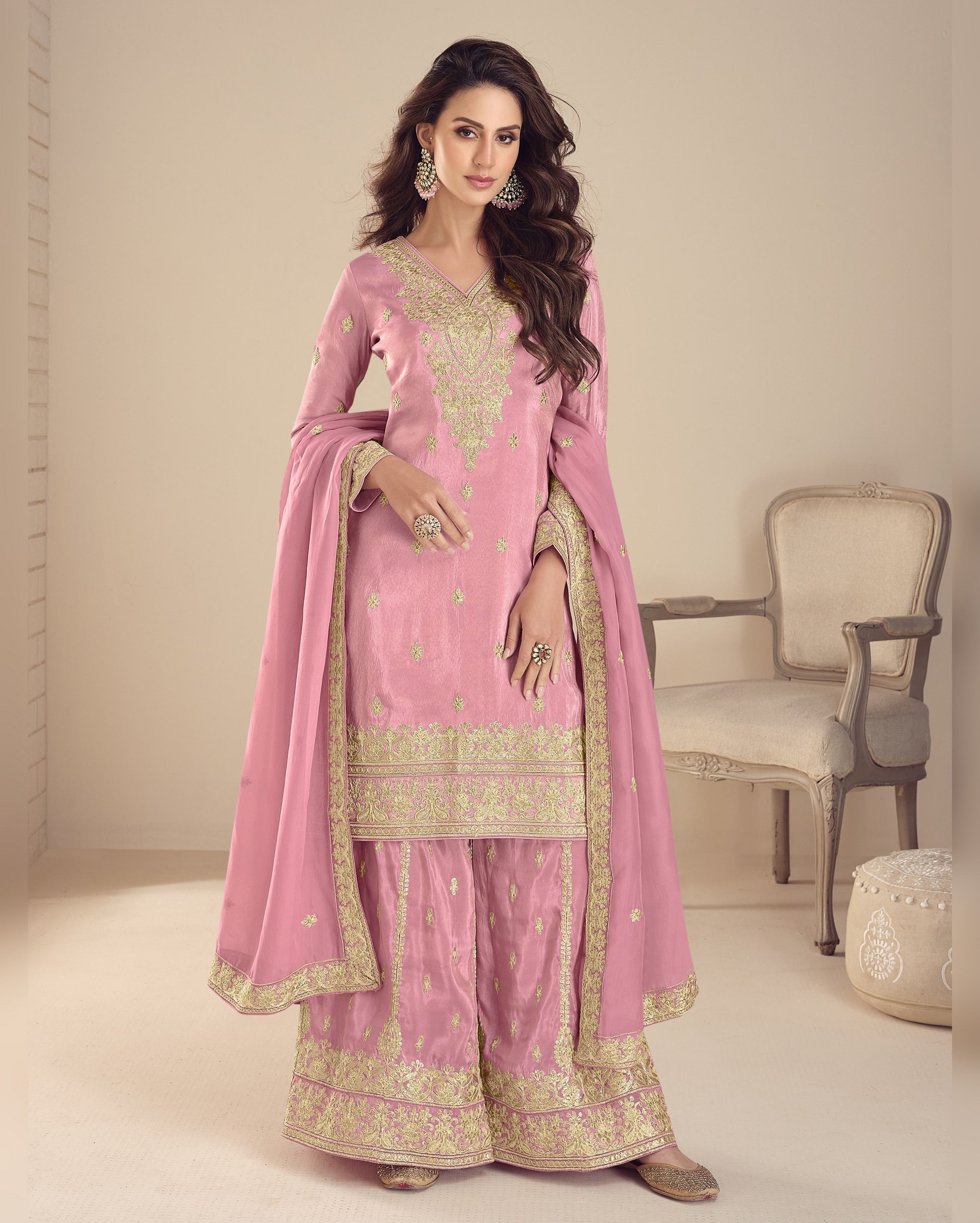 Woman wearing a pink traditional outfit with gold embroidery in a minimalistic room.