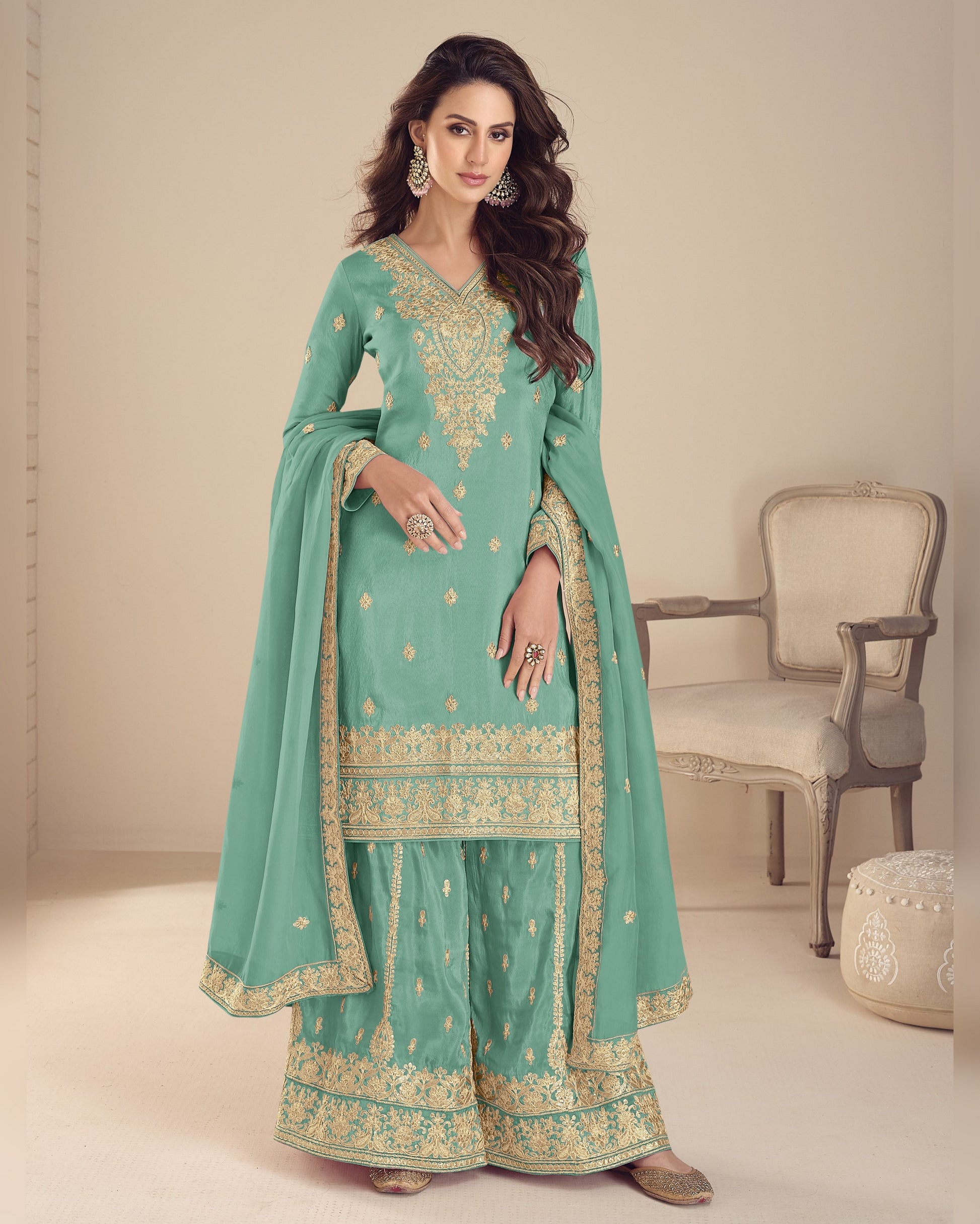 Woman wearing a light blue traditional outfit with gold embroidery in a minimalistic setting.