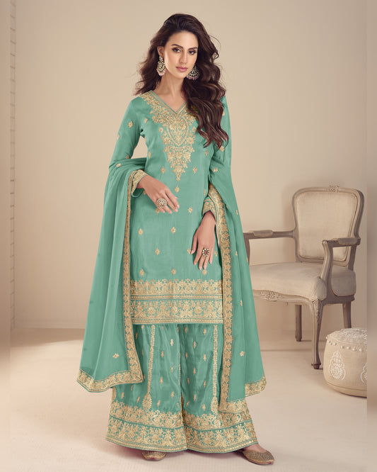 Woman wearing a light blue traditional outfit with gold embroidery in a minimalistic setting.