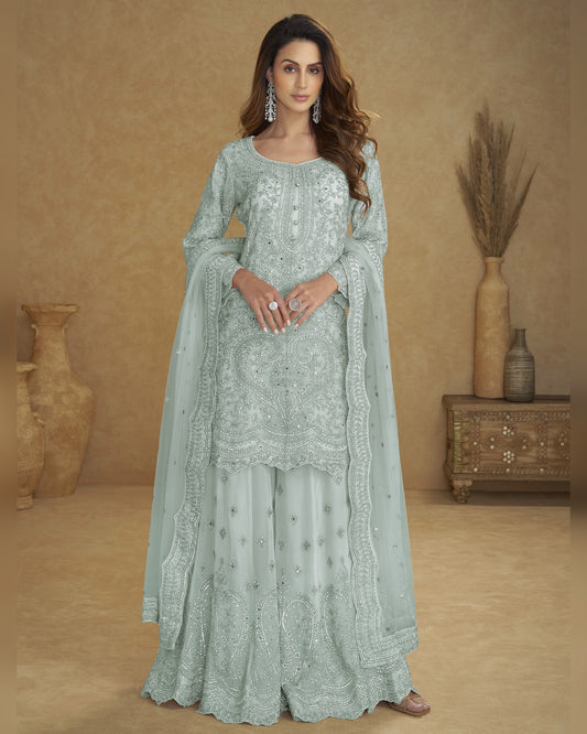 Woman wearing a light blue embroidered traditional outfit against a beige background