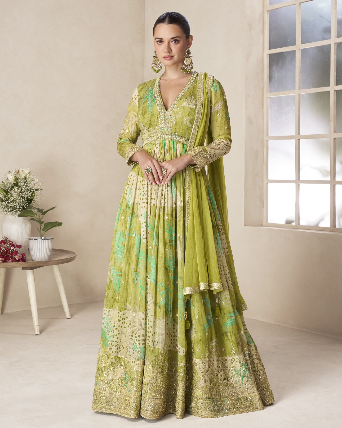 Woman wearing a green traditional outfit in a well-lit room with a window and small table.
