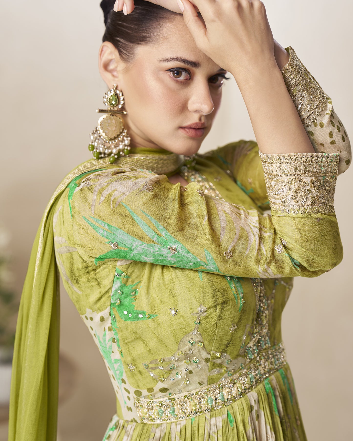 Woman wearing a green traditional outfit with intricate patterns and jewelry.