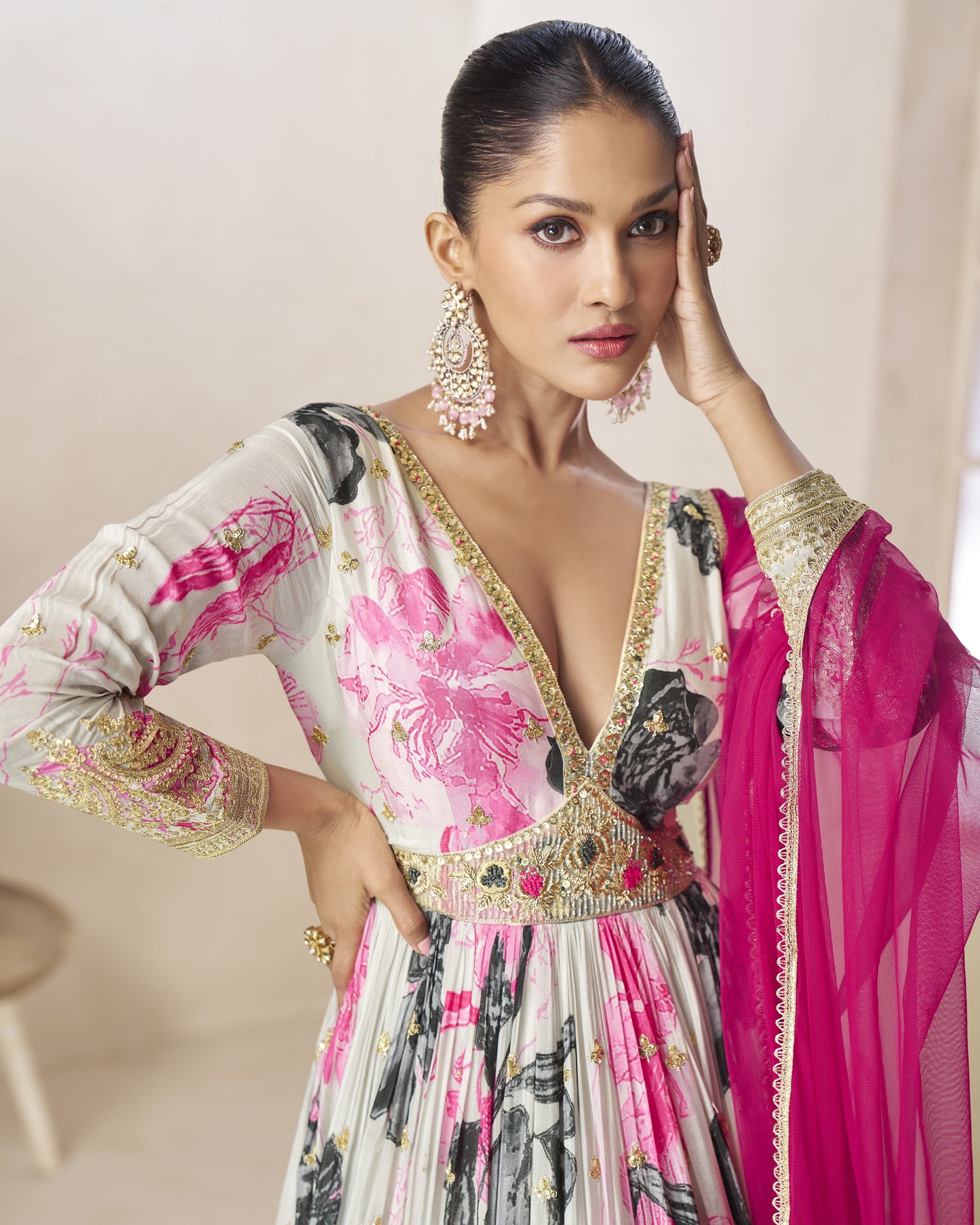 Woman wearing a traditional outfit with floral patterns and pink dupatta against a neutral background
