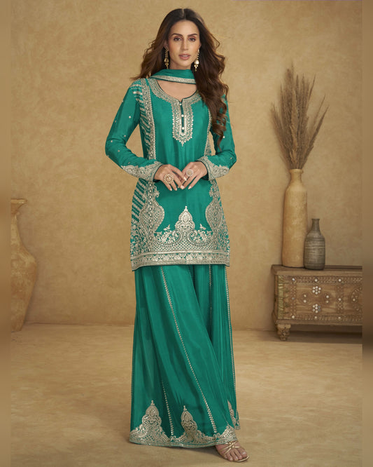 Woman wearing a green embroidered traditional outfit in a beige room.