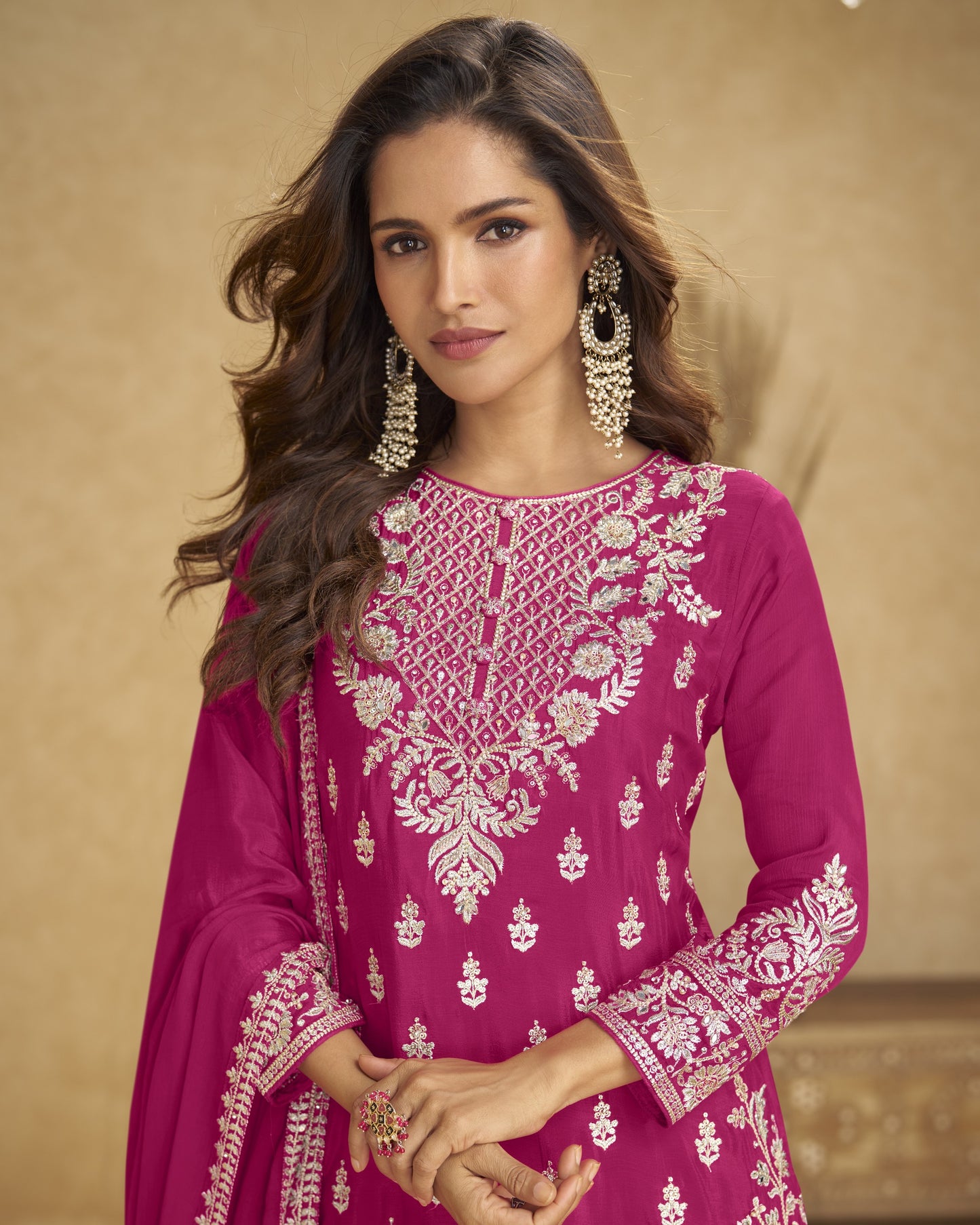 Woman wearing a pink embroidered traditional outfit with gold jewelry against a beige background