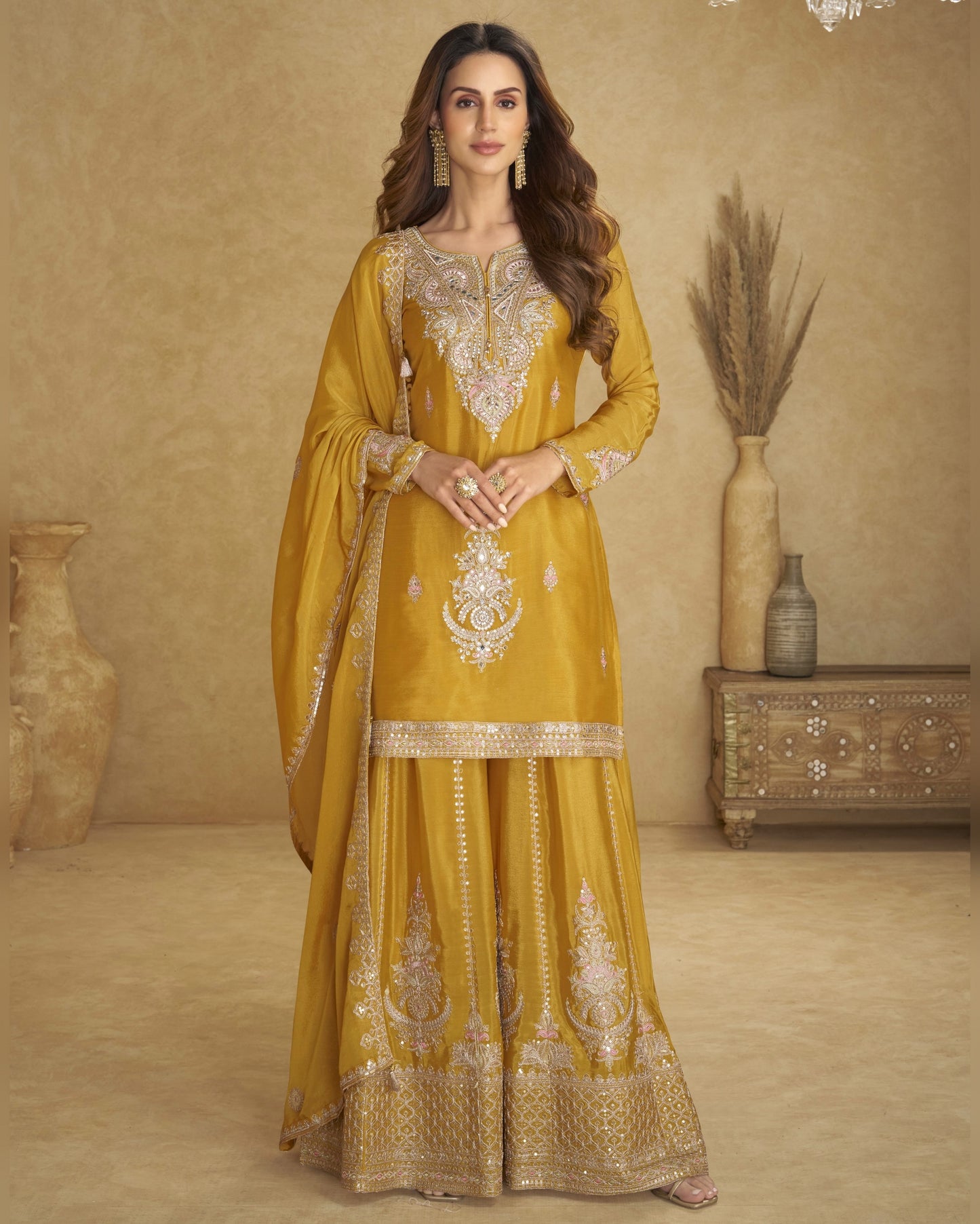 Woman in a yellow embroidered traditional outfit standing against a beige background