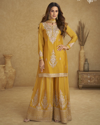 Woman wearing a mustard yellow embroidered traditional outfit in a decorated room.